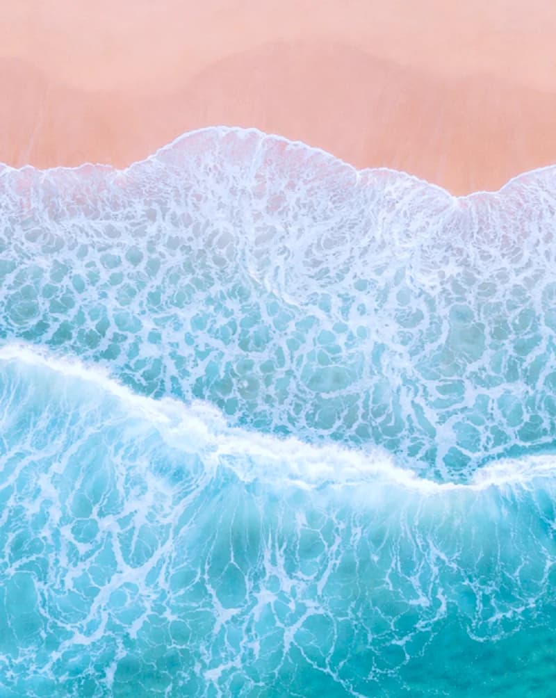 Foam edge of a wave washing over pink sand, seen from above
